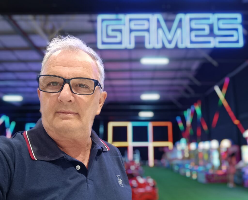 Retrato do LUIZÃO, criador do blog Mapa da Virada, em ambiente descontraído, com letreiro 'Games' ao fundo."